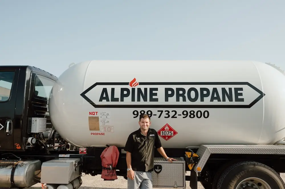 An Alpine Propane service tech standing in front of an Alpine Propane propane tank.